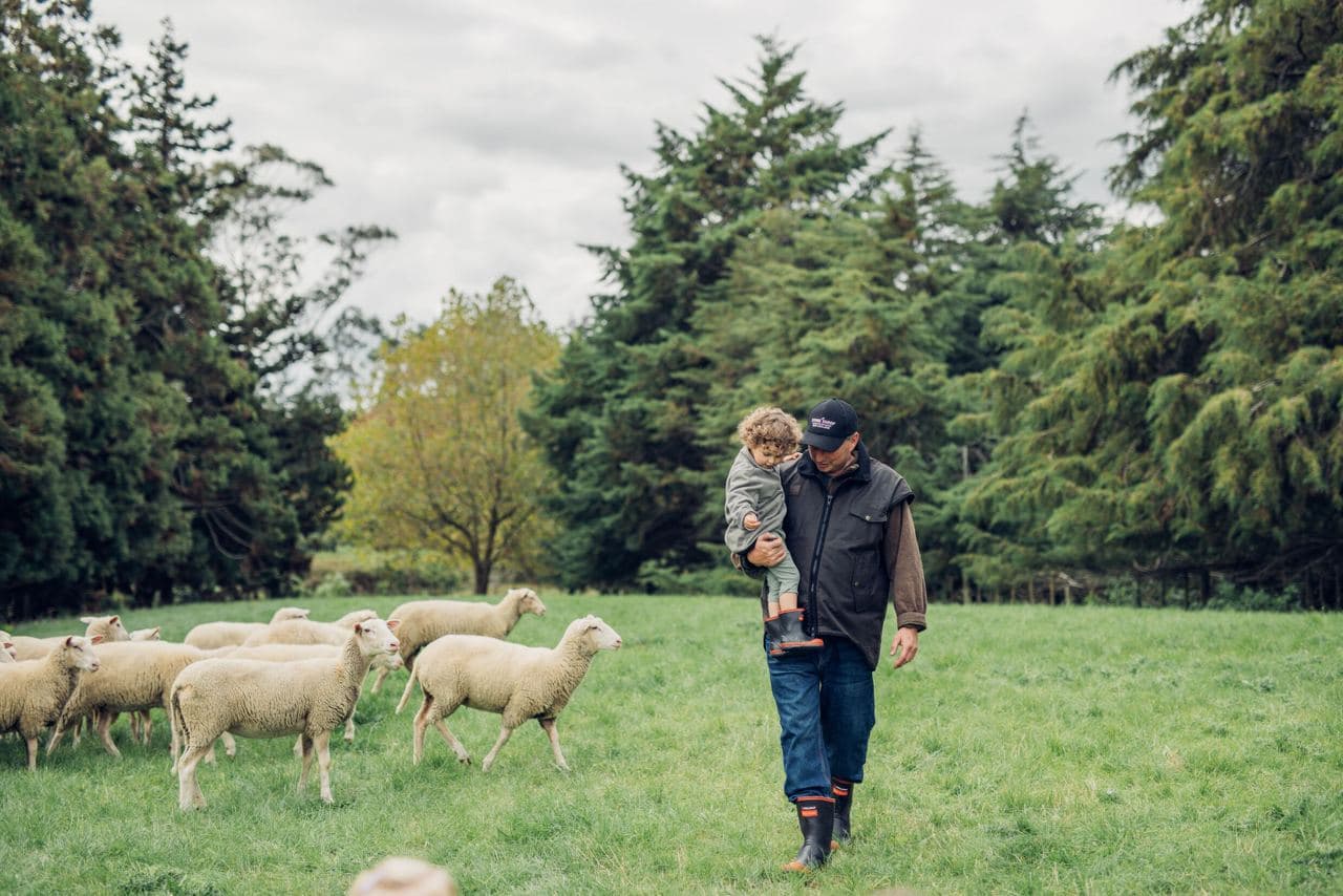 A sheep farmer holding a child in his arms